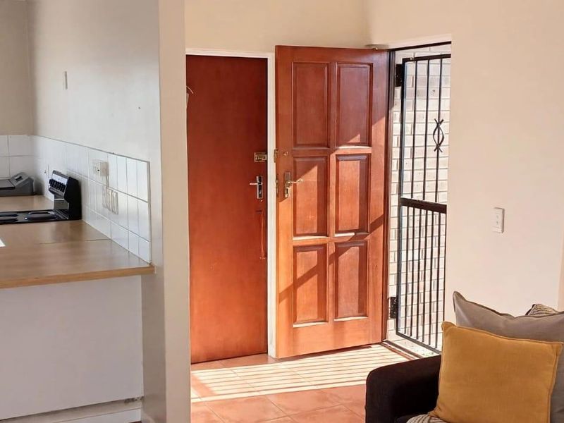 Open plan living area featuring tiled floors, a functional kitchen with laminate countertops, and direct access to the exterior through a secure entrance.