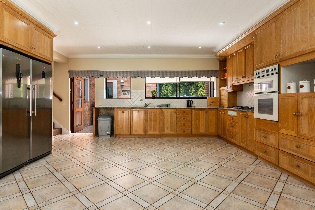 Spacious kitchen featuring extensive wooden cabinetry, built-in oven, gas cooktop, and tiled flooring, offering a functional layout with ample storage space.