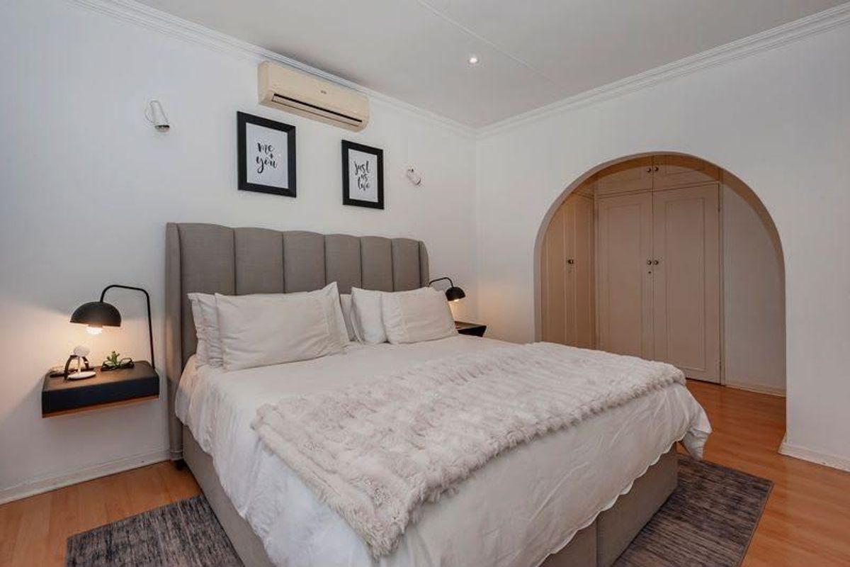 A well-maintained bedroom featuring laminate flooring, an arched entryway leading to built-in cupboards, and a wall-mounted split-system air conditioner.