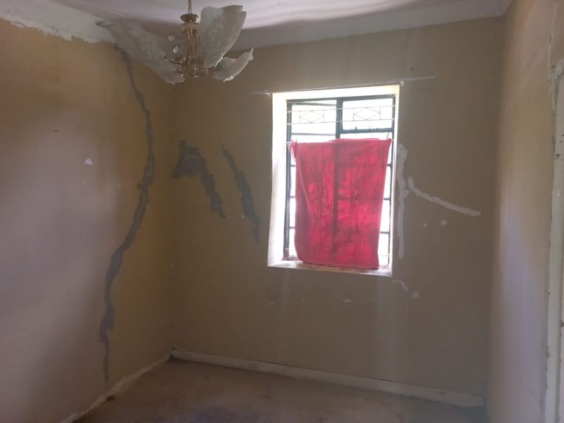 An empty bedroom requiring significant cosmetic renovation, featuring visible wall cracks and dated finishes, offering a blank canvas for complete refurbishment.
