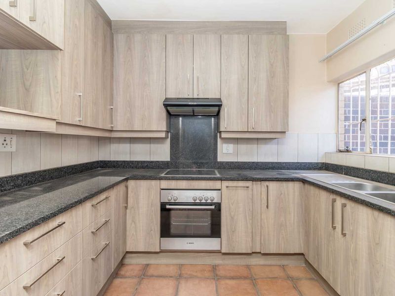 A functional kitchen featuring light wood-look cabinetry, granite countertops, a built-in oven with hob, and a double sink with tiled flooring.