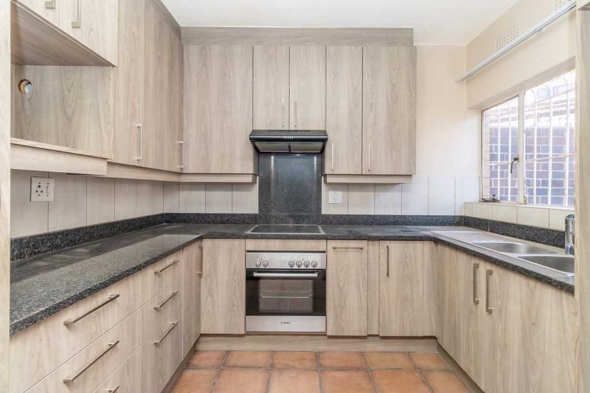 A functional kitchen featuring light wood-look cabinetry, granite countertops, a built-in oven with hob, and a double sink with tiled flooring.