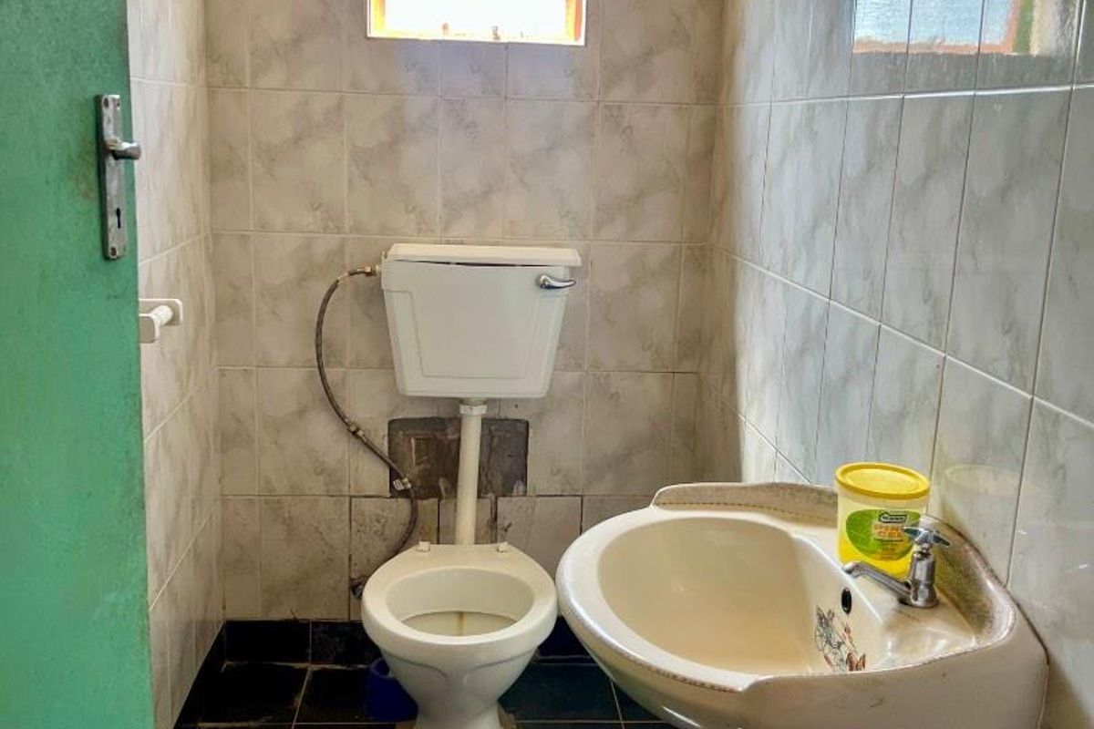 A compact bathroom featuring a pedestal basin and toilet, with tiled walls and flooring, requiring cosmetic updates and maintenance.