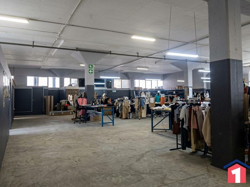 Spacious industrial utility area featuring exposed concrete ceilings, structural columns, and functional fluorescent lighting, suitable for manufacturing or storage operations.
