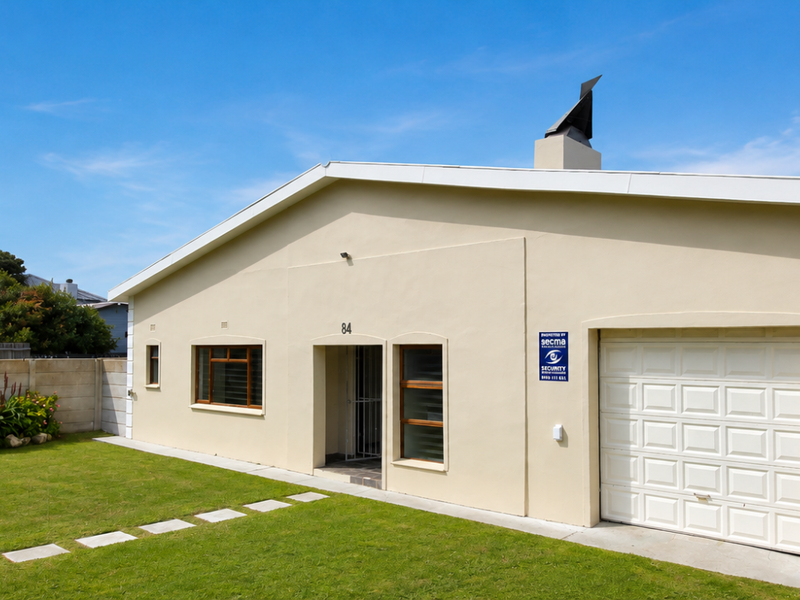 Front elevation of a single-story house featuring a garage, paved walkway, and a well-maintained lawn with perimeter boundary walling.