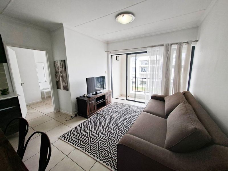 A bright living room featuring tiled flooring and a sliding glass door providing access to a private balcony.