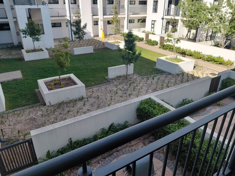 An elevated view of a well-maintained communal garden area featuring raised concrete planters, manicured lawn, and paved pathways within an apartment complex.