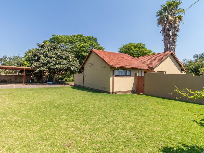 A view of the rear exterior featuring a well-maintained lawn, a tiled roof structure, and a covered carport area.