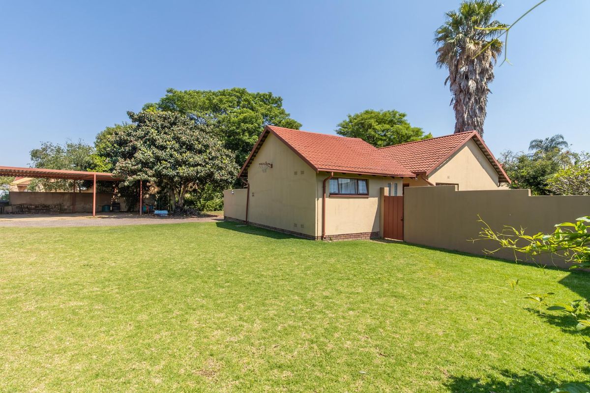 A view of the rear exterior featuring a well-maintained lawn, a tiled roof structure, and a covered carport area.