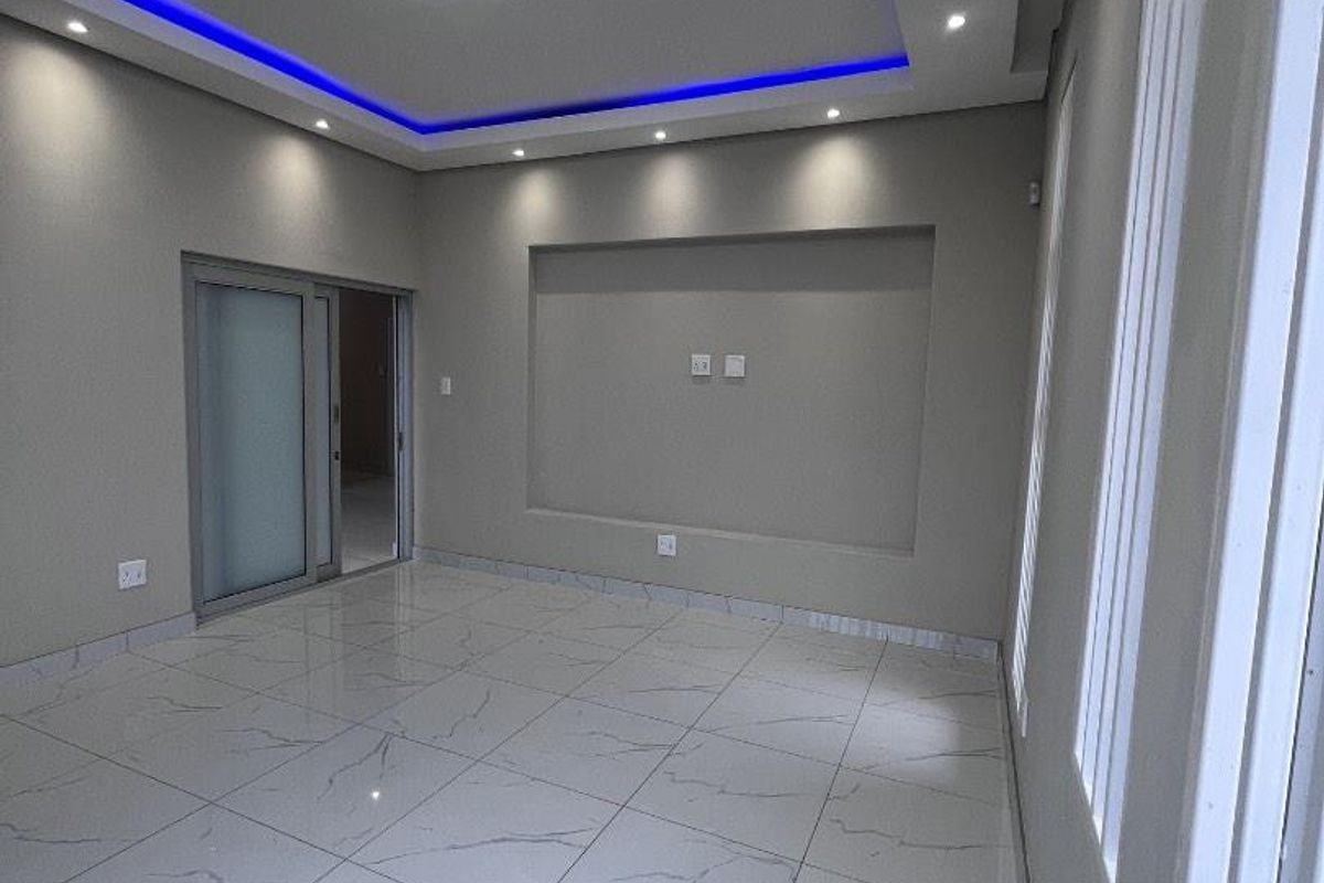 A modern, empty living room featuring polished marble-look floor tiles, recessed ceiling lighting with blue LED accents, and a built-in wall niche.
