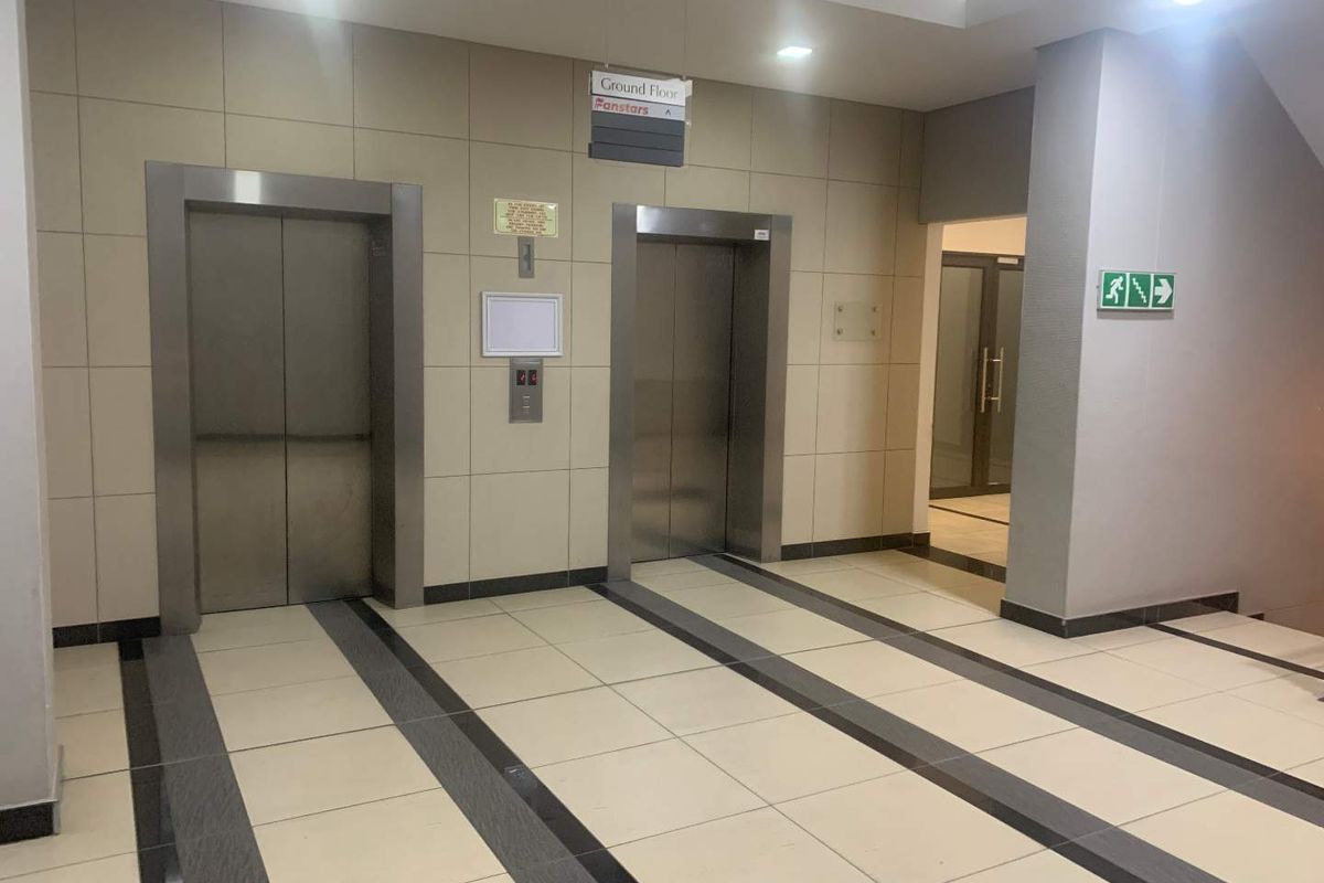 A clean and modern office building lobby featuring dual stainless steel elevators, tiled flooring, and recessed lighting.