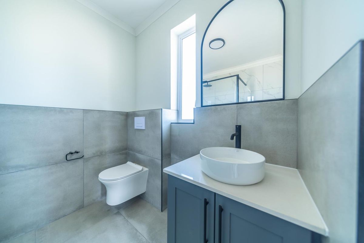 Modern bathroom featuring a wall-hung toilet, vanity with vessel sink, black fixtures, and an arched mirror against contemporary grey tiling.