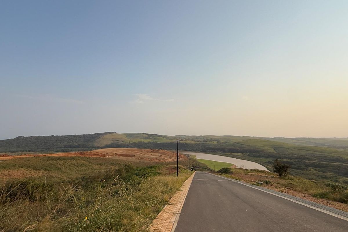 A view of a paved residential road leading through a developing landscape with rolling hills and a nearby river.