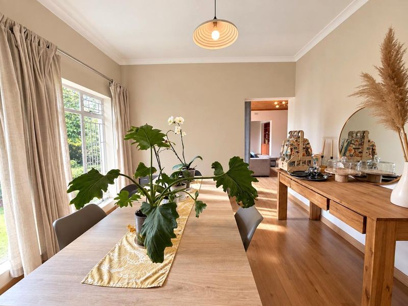 A bright and well-maintained dining room featuring laminate flooring, neutral wall tones, and a large window providing natural light.
