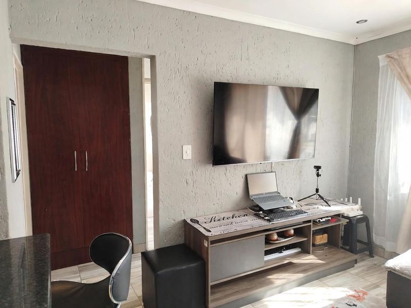 A living room featuring textured walls, tiled flooring, and a built-in cupboard, providing a functional and neutral living space.