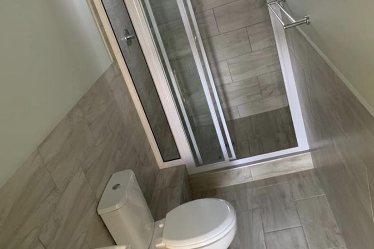 A modern, compact bathroom featuring a walk-in shower enclosure, wall-mounted basin, and toilet, finished with neutral wood-look floor and wall tiles.