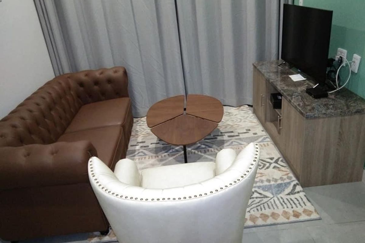 A compact hotel living area featuring tiled flooring and neutral curtains, providing a functional space for guests.