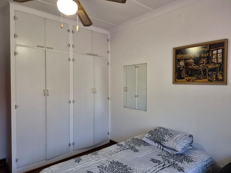 A bedroom featuring floor-to-ceiling built-in cupboards and a ceiling fan, offering functional storage space.