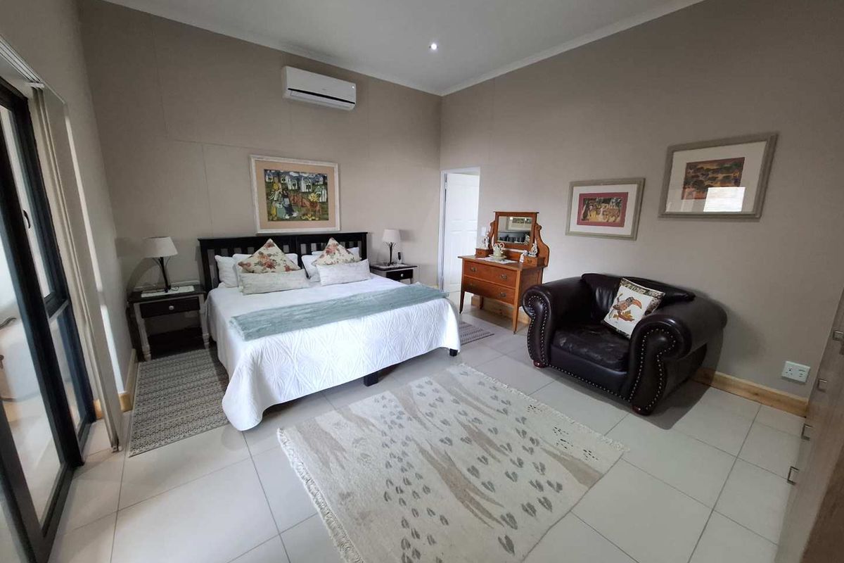 Spacious bedroom featuring tiled flooring, neutral wall finishes, and a wall-mounted air conditioning unit with direct access to an outdoor area.