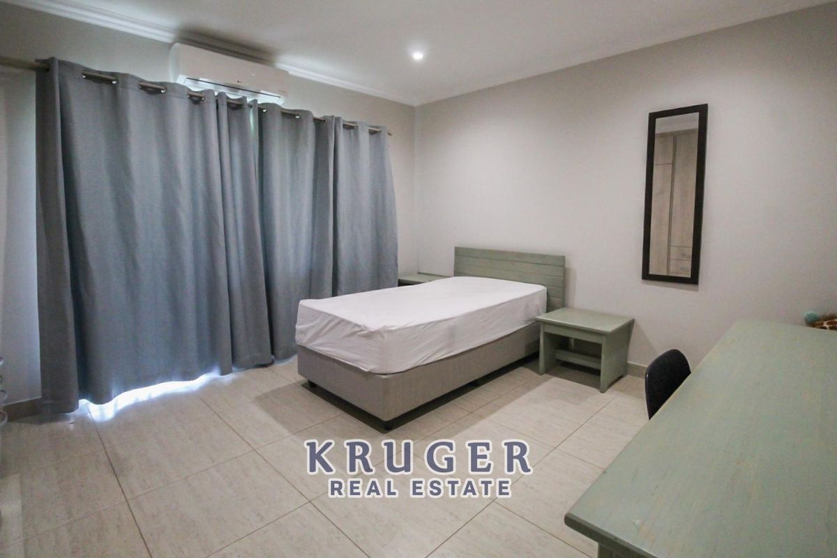 A well-maintained bedroom featuring tiled flooring, a wall-mounted air conditioning unit, and neutral wall finishes.