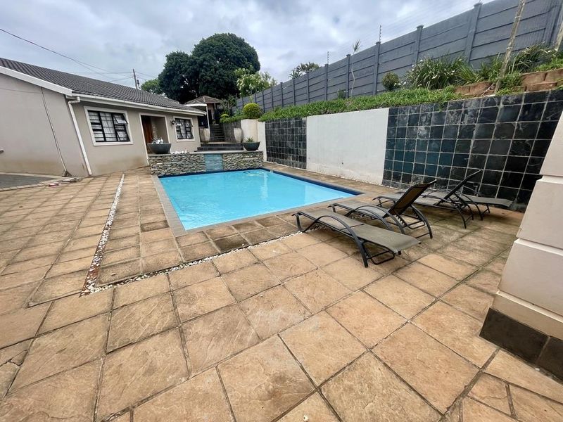 Outdoor pool area featuring a paved patio, a stone-clad water feature, and a high perimeter wall for privacy.