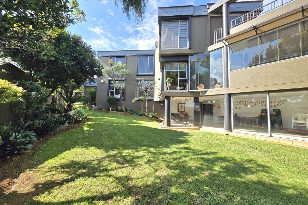 A multi-story residential property featuring large glass windows, a modern architectural design, and a well-maintained rear garden with lawn and mature trees.