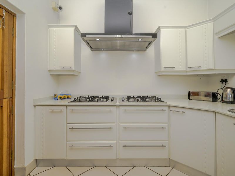 A clean, modern kitchen featuring white cabinetry, stone countertops, a gas hob with a stainless steel extractor fan, and tiled flooring.