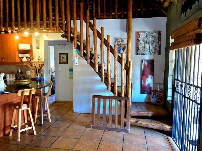 Open plan living area featuring a rustic thatched roof, wooden staircase with balustrade, tiled flooring, and a kitchen with granite countertops.