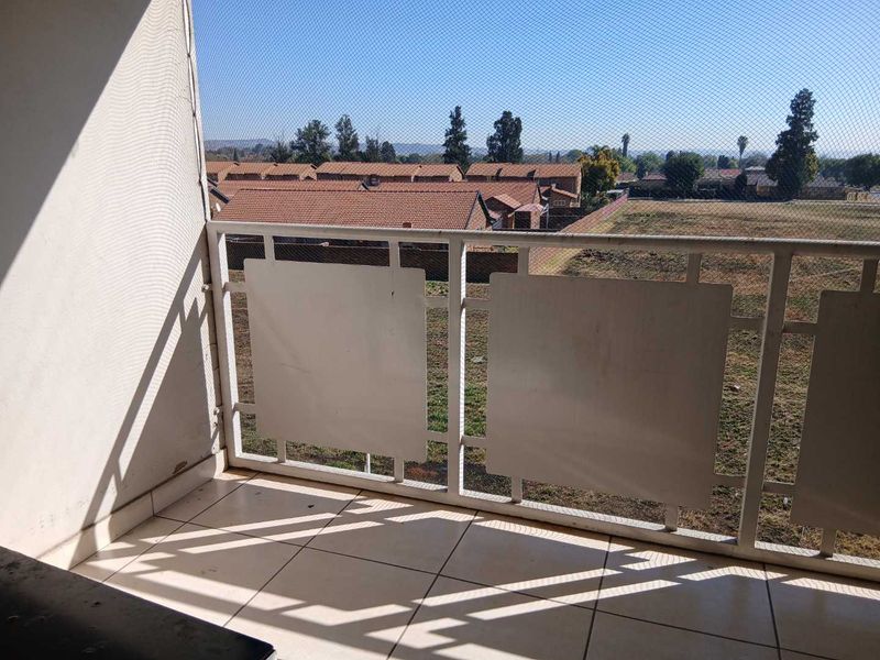 A functional balcony featuring tiled flooring and a metal balustrade with safety netting, offering an open view of the surrounding residential area.