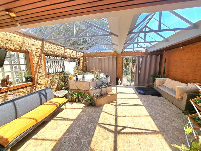 A spacious enclosed patio featuring a glass roof, stone wall finishes, tiled flooring, and a built-in spa area, perfect for year-round relaxation.