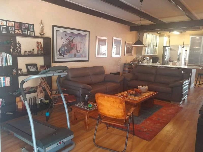 Open-plan living area featuring exposed ceiling beams, laminate flooring, and a connected kitchen with a breakfast island.