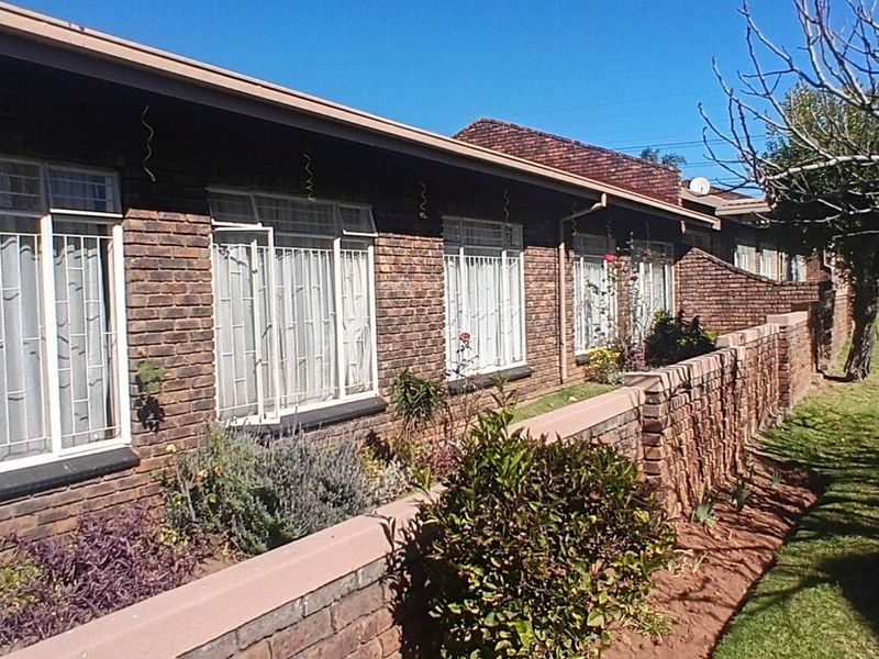 Rear exterior view of a face-brick townhouse featuring security bars on windows and a low brick retaining wall bordering the garden area.
