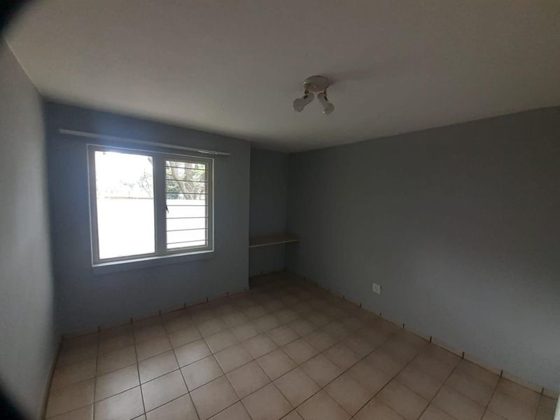 An empty bedroom featuring tiled flooring, a built-in desk, and a window fitted with security bars.