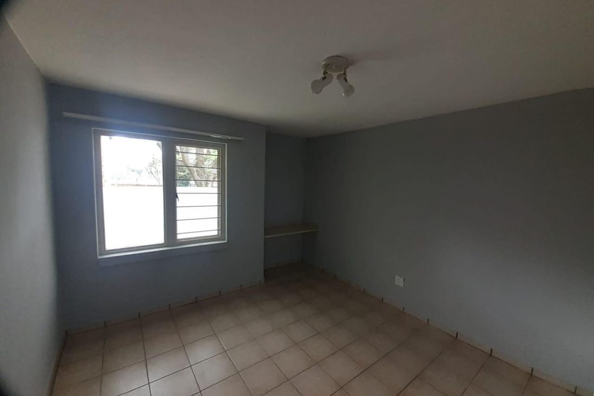 An empty bedroom featuring tiled flooring, a built-in desk, and a window fitted with security bars.