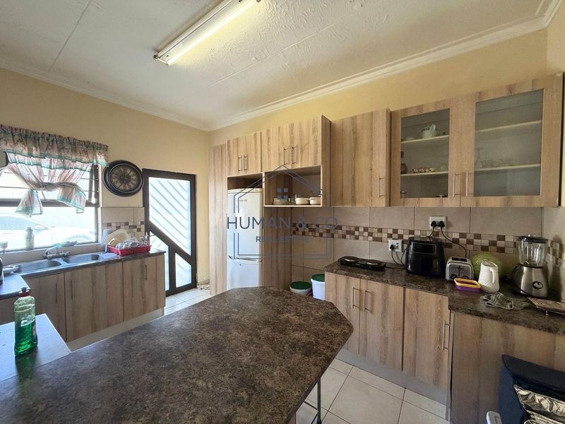 Functional kitchen featuring wood-look laminate cabinetry, durable laminate countertops, tiled backsplash, and tiled flooring with ample storage space.