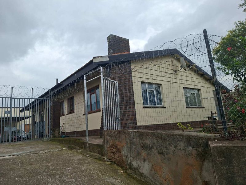 Front exterior view of a single-story house featuring a brick chimney, concrete driveway, and extensive security fencing with razor wire.
