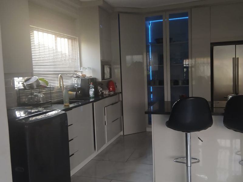 Modern kitchen featuring high-gloss cabinetry, stone countertops, integrated display lighting, and large format floor tiles.
