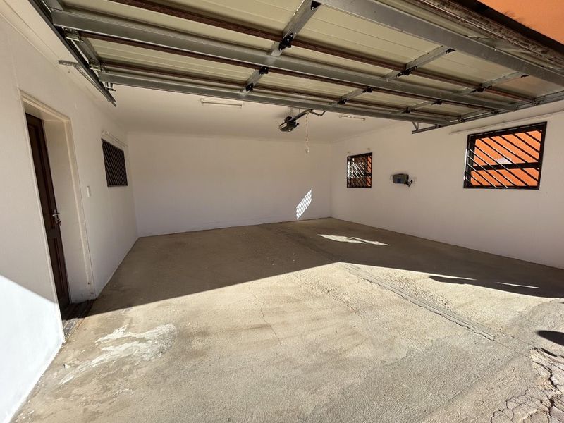 A spacious, empty double garage featuring a sectional door, security-barred windows, and a concrete floor.