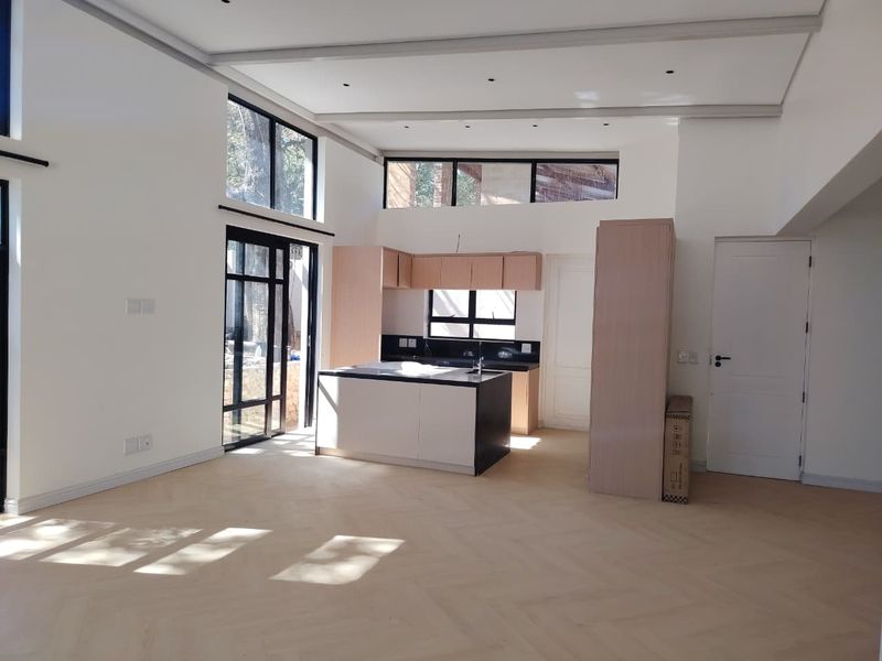 Spacious open-plan living and kitchen area featuring modern cabinetry, a central island, herringbone flooring, and large windows providing ample natural light.