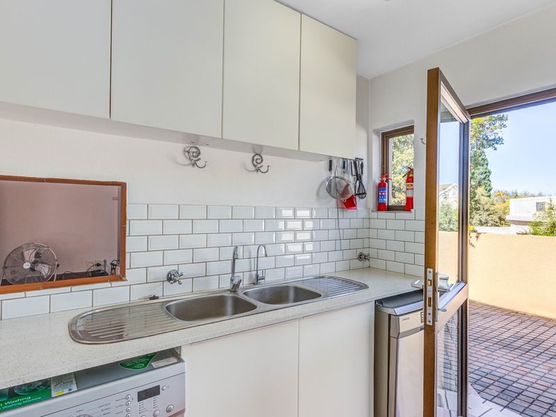 A functional laundry area featuring a double stainless steel sink, subway tile backsplash, and direct access to an outdoor patio space.