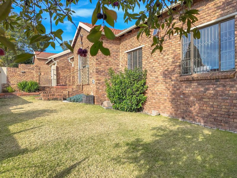 A well-maintained rear exterior view of a facebrick cluster home featuring a private lawn, tiled roof, and secure window bars.