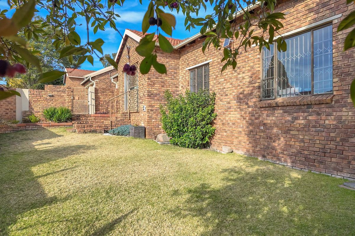 A well-maintained rear exterior view of a facebrick cluster home featuring a private lawn, tiled roof, and secure window bars.
