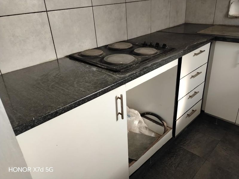 A kitchen area featuring a built-in electric hob, dark laminate countertops, and white cabinetry with a missing appliance space.