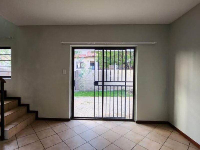 An empty living room featuring tiled flooring, a staircase with a metal railing, and a sliding glass door leading to the exterior.