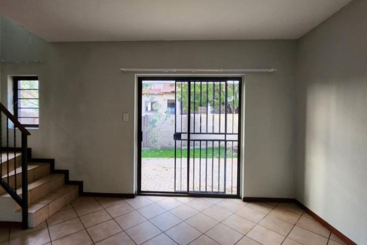 An empty living room featuring tiled flooring, a staircase with a metal railing, and a sliding glass door leading to the exterior.