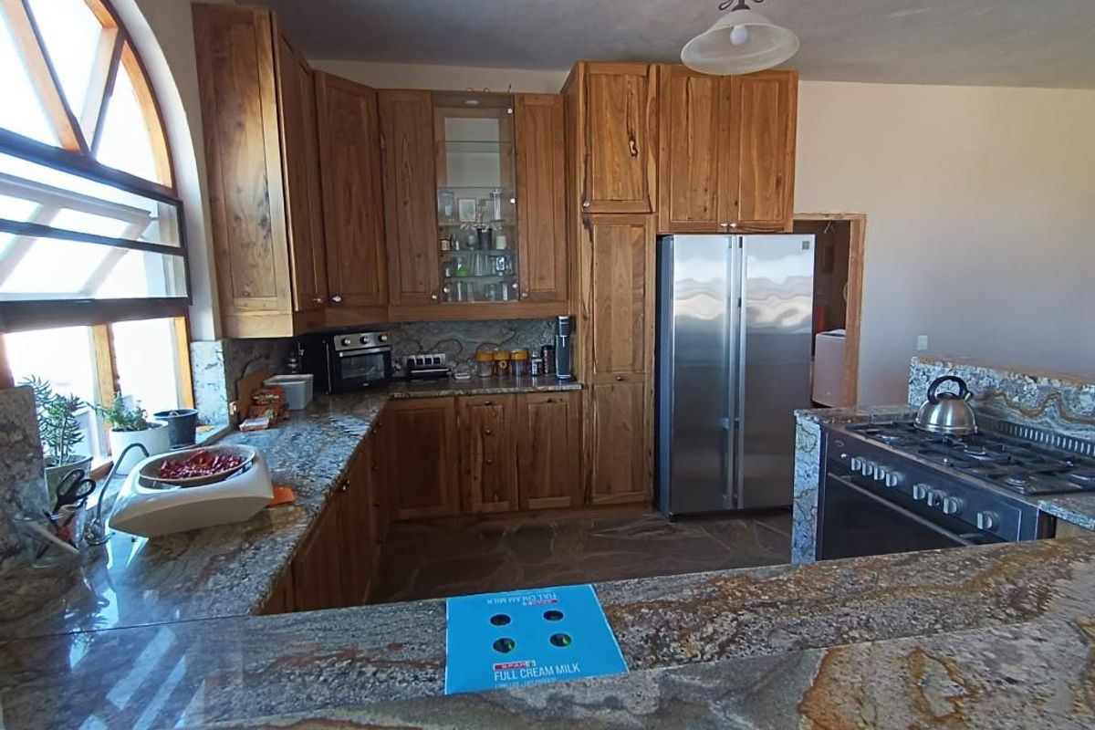 Spacious kitchen featuring rustic wooden cabinetry, granite countertops, a built-in gas hob, and a distinctive arched window providing natural light.
