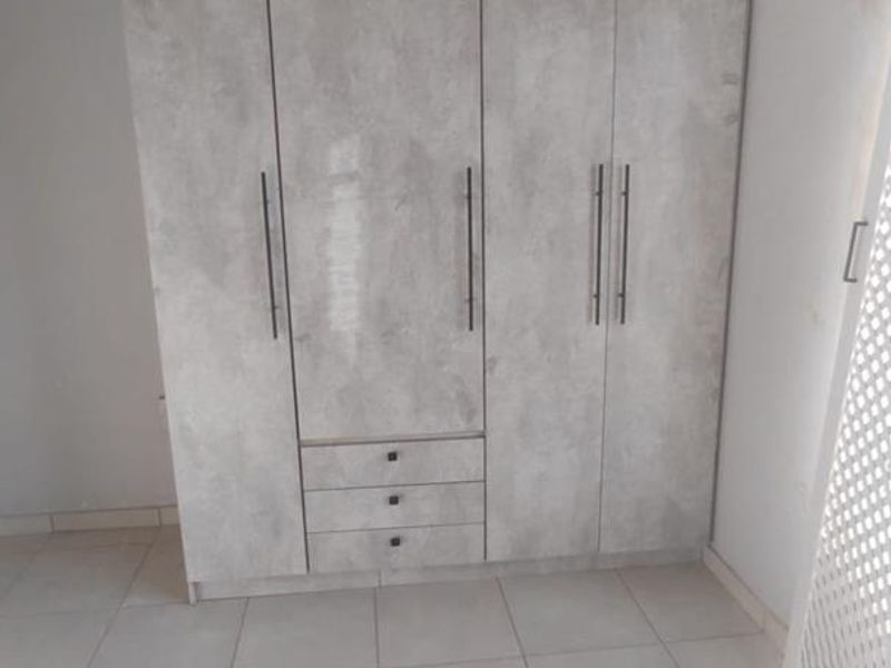 A bedroom featuring a modern grey-toned built-in wardrobe with integrated drawers and neutral tiled flooring.