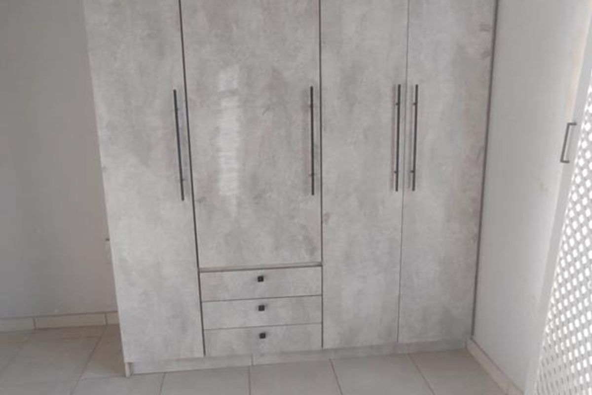 A bedroom featuring a modern grey-toned built-in wardrobe with integrated drawers and neutral tiled flooring.