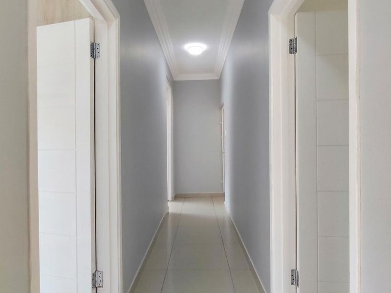 A clean, well-maintained hallway featuring neutral grey walls, tiled flooring, and crisp white door frames with modern internal doors.