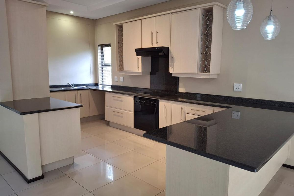 A spacious, modern kitchen featuring granite countertops, ample built-in cabinetry, an integrated oven with extractor fan, and sleek tiled flooring.